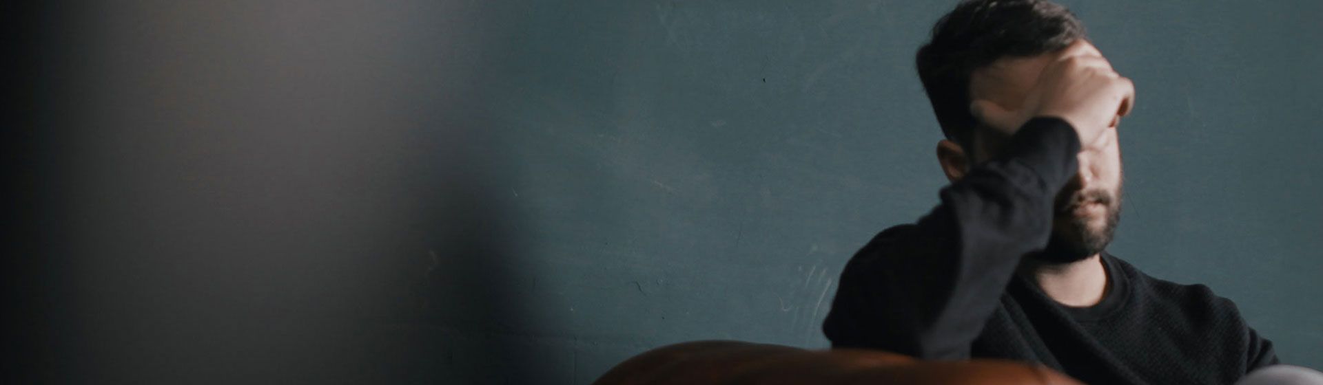Man in a dark room, holding his head in pain.