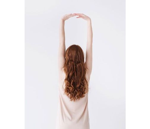 Woman stretching her arms above her head, back held straight.