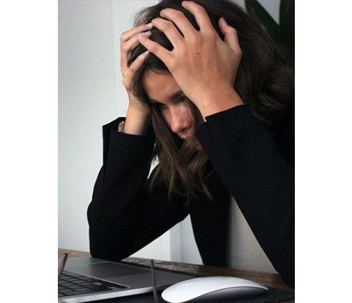 Woman holding her head in frustration and stress while looking at her laptop.