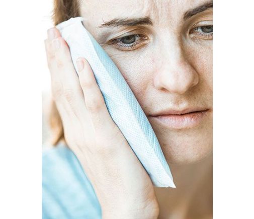Woman holding an ice pack to her jaw in pain.
