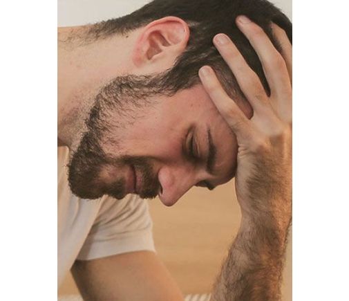 Man in pajamas, getting out of bed, looking pained and unhappy.