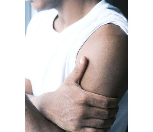 Man looking out a window, holding his arm in pain