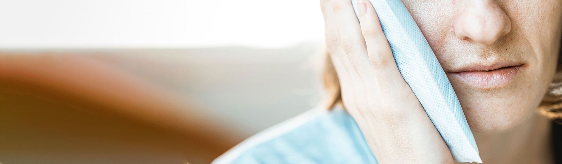 Woman holding an ice pack to her jaw in pain.